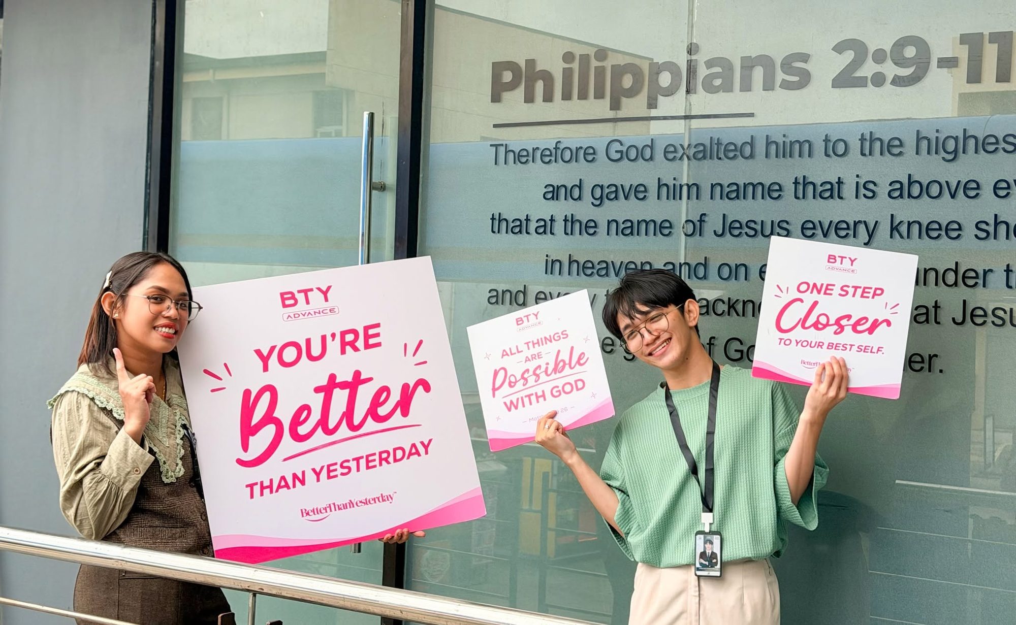 Two BTY Advance team members holding You're Better Than Yesterday and One Step Closer signs